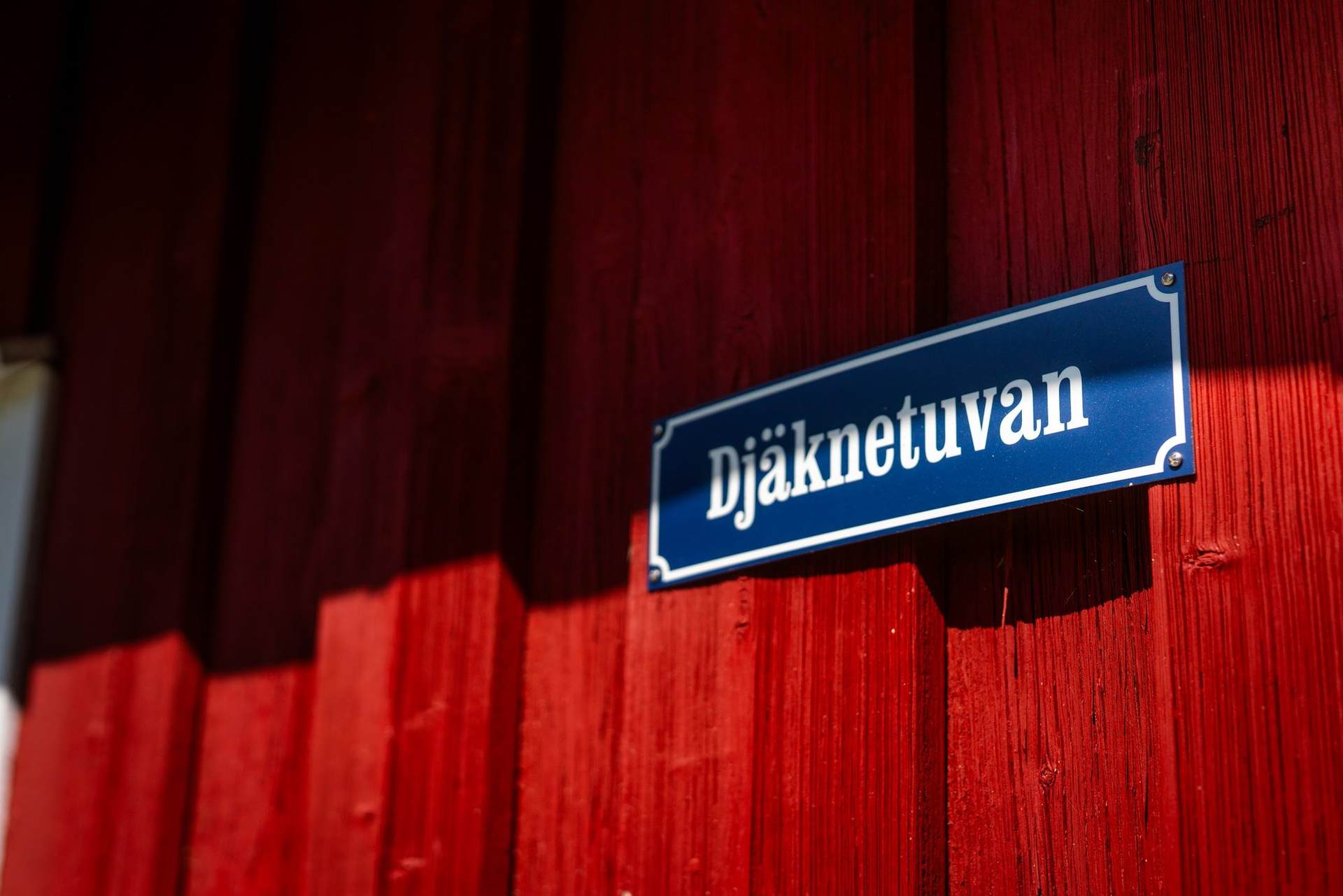 Red painted timber wall with the blue enamel name plate Djäknetuvan