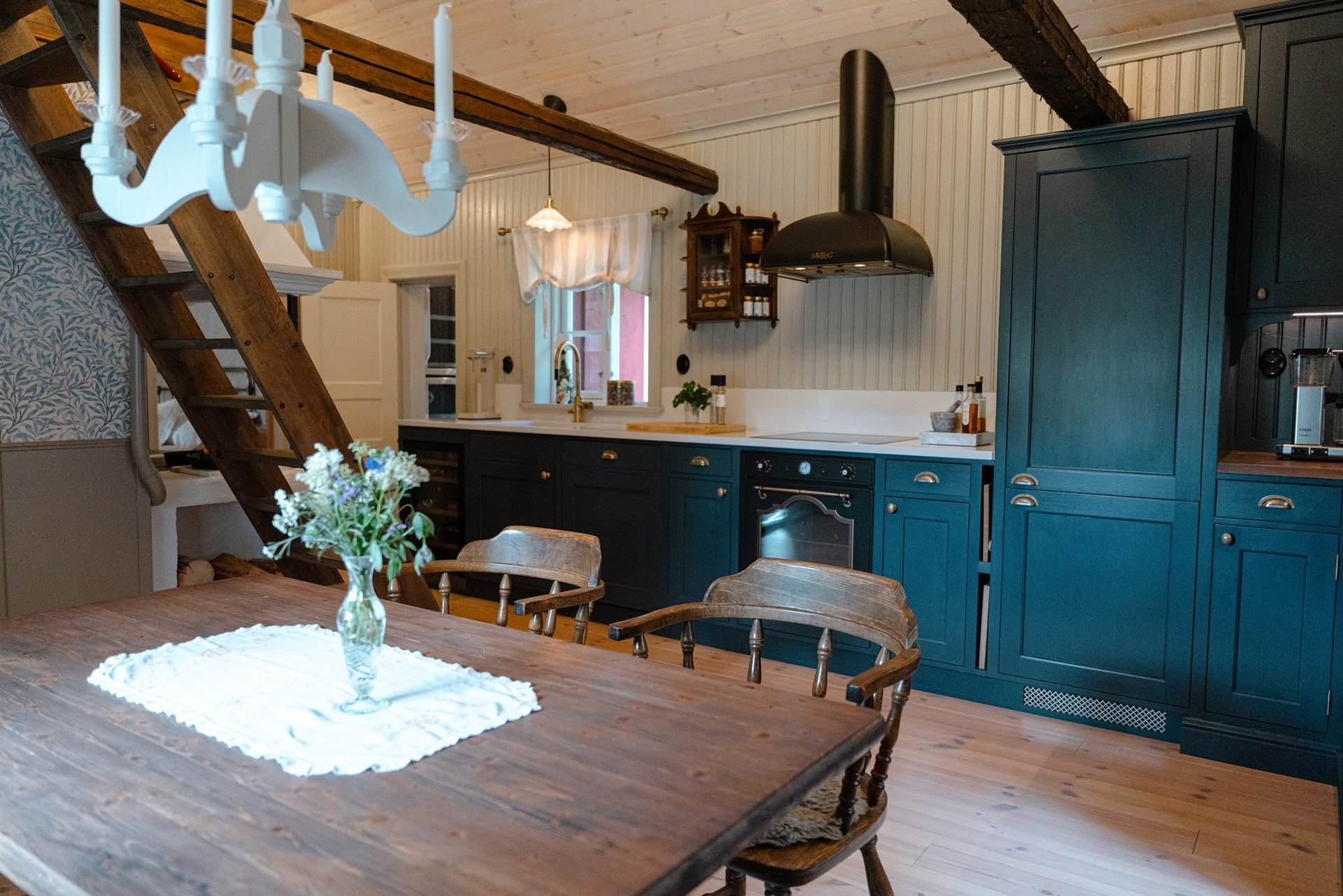 Kitchen with dark blue cabinets, a long wooden table and a white chandelier